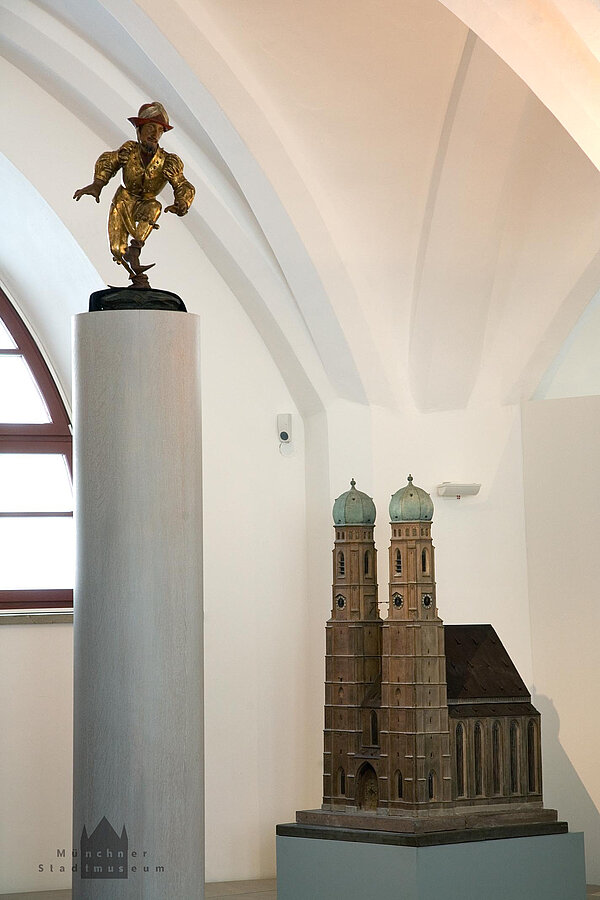 Ausstellungsansicht mit Modell der Frauenkirche und Holzfigur eines Moriskentänzers auf einer Säule.
