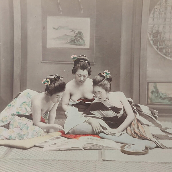 In einem Innenraum sitzen drei Damen auf dem Boden und betrachten ein fotografisches Album