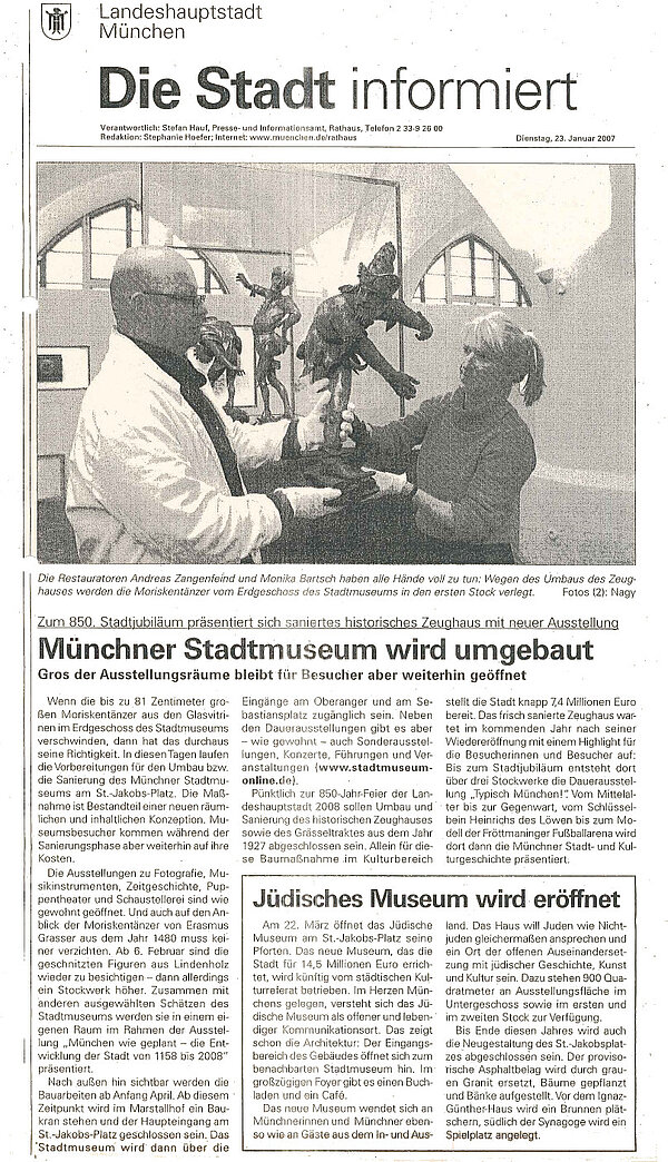 Zeitungsartikel zum Umbau des Münchner Stadtmuseums mit Foto, auf dem ein Mann und eine Frau zu sehen sind, die eine Holzfigur aus einer Vitrine heben.