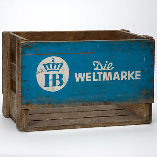 Holzkiste mit blauer Seitenwand und „Hofbräuhaus“-Logo, daneben die Aufschrift „Die Weltmarke“.