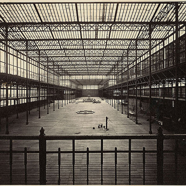 Historische schwarz-weiß-Fotografie mit Innenansicht einer riesigen Halle aus Stahl und Glas. 