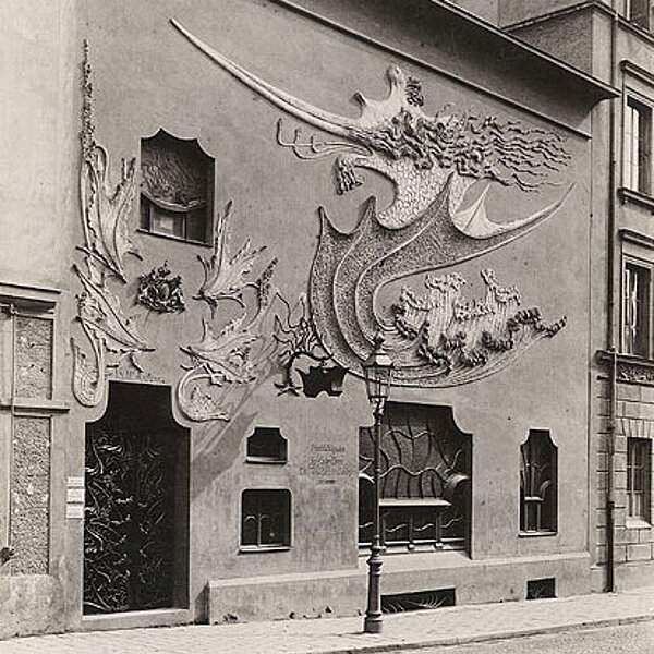 Historische schwarz-weiß-Fotografie einer Gebäudefassade mit aufwändigen großflächigen Verzierungen.
