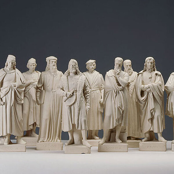 Elf Standfiguren in weiß, die verschiedene Künstler darstellen.