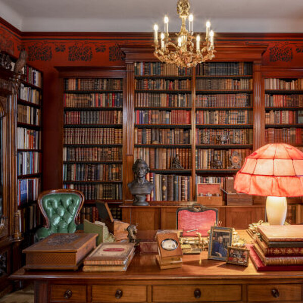 Kleiner Bibliotheksraum mit roten Wänden, vielen alten Büchern und großem Schreibtisch