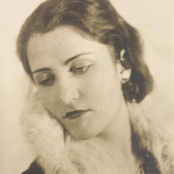 Porträt einer jungen Frau mit dunklem halblangem Haar und weißem Pelzkragen, nach links unten blickend