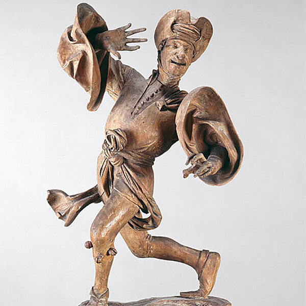 Tanzende männliche unbemalte Holzfigur, mit weiten Ärmeln und auffälligem Hut.