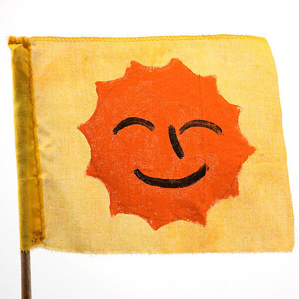 Gelbe Fahne mit orangener Sonne mit lachendem Gesicht und geschlossenen Augen.