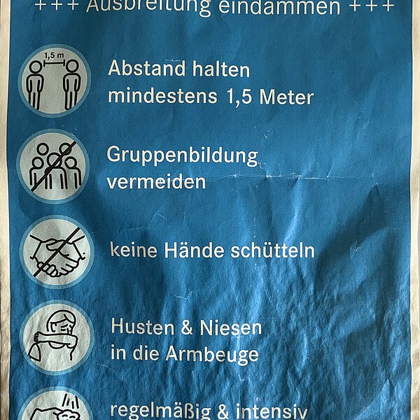 Zerknittertes Plakat der Landeshauptstadt München mit verschiedenen Piktogrammen zu Hygienemaßnahmen.