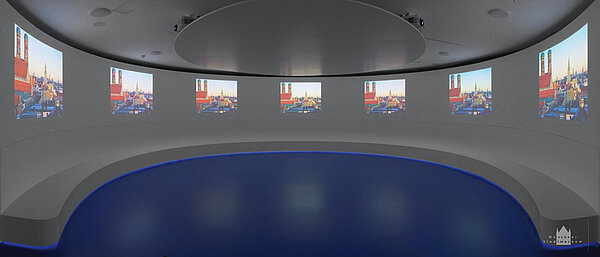 Raumansicht eines rundes Kinoraums mit mehreren parallelen Videoprojektionen an der Wand.