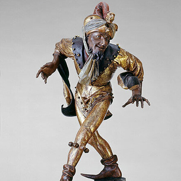 Tanzende männliche Holzfigur, überwiegend in gold und rot bemalt.